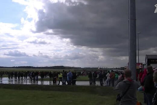 Eine Menschenmenge versammelt sich bei bewölktem Himmel neben einem Crepes-Stand auf einem offenen Gelände.