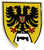 Ein Wappen zeigt einen schwarzen Doppeladler mit roten Krallen auf gelbem Hintergrund, verziert mit einem Schild in der Mitte.