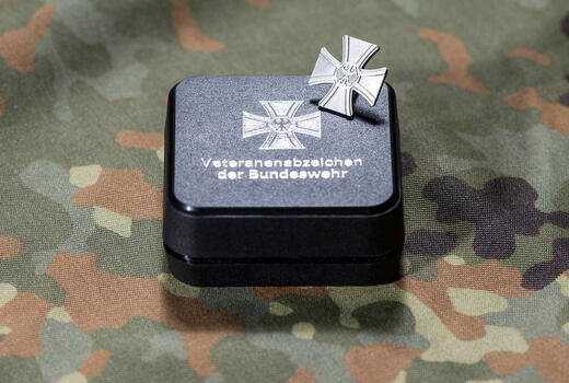 Ein Bundeswehr-Veteranenabzeichen liegt auf einer Tarnstoffunterlage neben seiner Präsentationsbox.