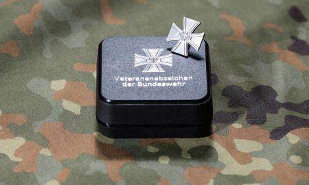 Ein Bundeswehr-Veteranenabzeichen liegt auf einer Tarnstoffunterlage neben seiner Präsentationsbox.