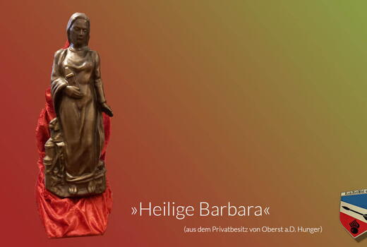 Eine Statue der Heiligen Barbara steht auf einem roten Tuch vor einem farbigen Hintergrund.
