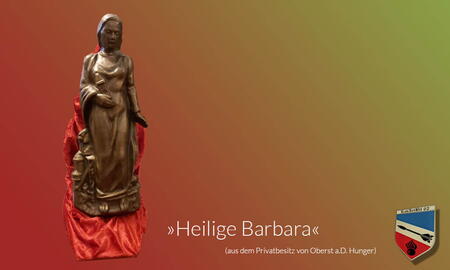 Eine Statue der Heiligen Barbara steht auf einem roten Tuch vor einem farbigen Hintergrund.