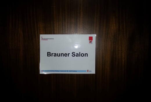 Ein Schild mit der Aufschrift "Brauner Salon" hängt an einer dunklen Holzwand im Bundeswehrkrankenhaus Hamburg.