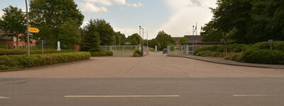 Eine breite Einfahrt führt zur Dithmarsen-Kaserne, umgeben von Bäumen und einem klaren Himmel.