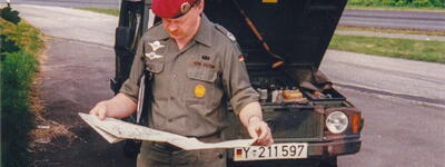Ein Soldat in Uniform betrachtet eine Karte vor einem Geländewagen mit geöffnetem Motorhaube am Straßenrand.
